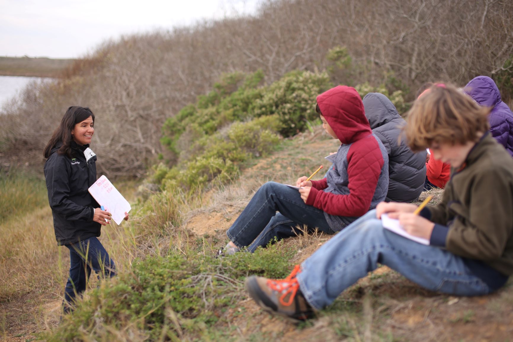 students writing in journals while sitting on a coastal hillside